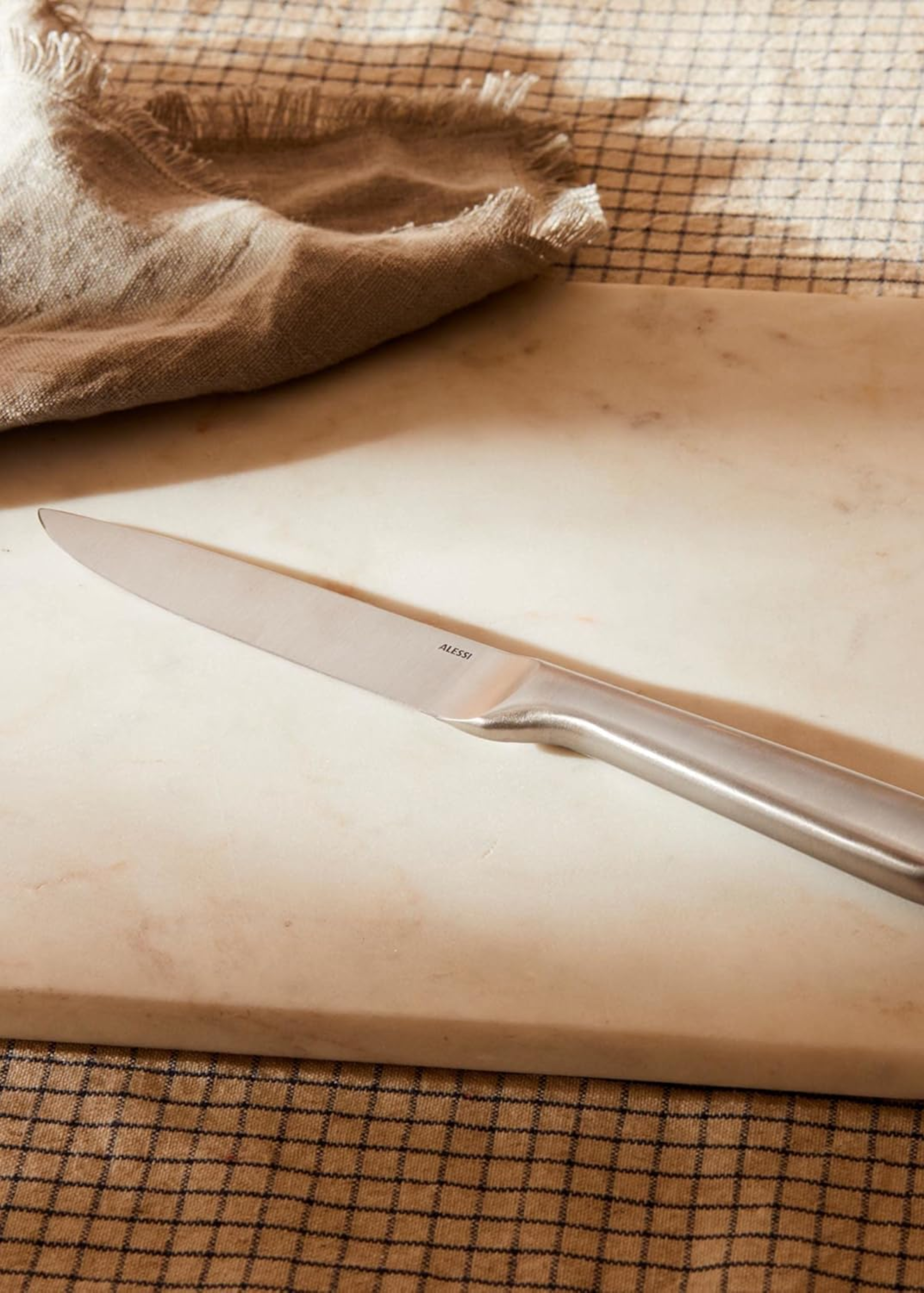A steel knife on a solid cutting board with a grid wash cloth