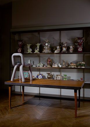 Modern white chair on table with old ornaments on shelves in background