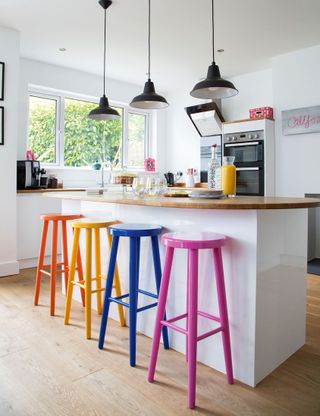 A white kitchen in an open plan living area with an island and colorful bar stools