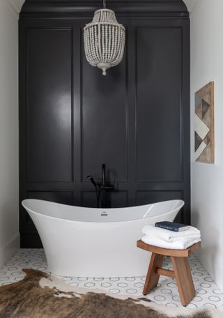 A bathroom with one black panelled wall behind a freestanding bath, with white and black patterned floor tiles