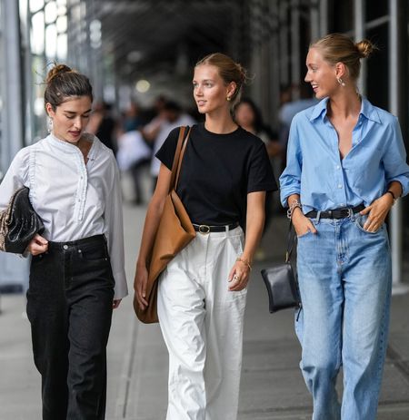 NEW YORK, NEW YORK - SEPTEMBER 13: A guest (L) wears a white striped print pattern shirt, black denim pants, a brown shiny snake print pattern puffy handbag, black denim pants, brown camel shiny leather pointed loafers, a guest (M) gold earrings, a black t-shirt, a camel shiny leather oversized shoulder bag, a black shiny leather belt, gold rings, a gold bracelet, white large pants, flip flop, a guest (R) wears gold earrings, a baby blue shirt, a black shiny leather belt, a black shiny leather zipper clutch, a black watch, silver rings, blue denim large pants, navy blue suede pointed pumps heels shoes , outside COS, during New York Fashion Week, on September 13, 2022 in New York City. (Photo by Edward Berthelot/Getty Images)