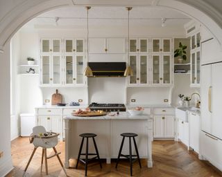 A white transitional kitchen with a kitchen island with black bar stools and a high chair