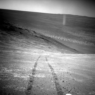 A black and white photo of a rocky terrain with black tracks visible on the ground