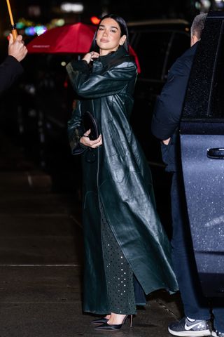 A photo of Dua Lipa wearing a dark green leather trench and a sheer Alaïa maxi dress for her appearance on The Late Show with Stephen Colbert.