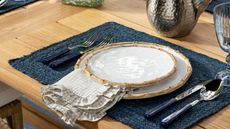 Bamboo plates styled alongside gingham napkin linen, navy placemat, and coordinating navy flatware atop of a wooden dining table