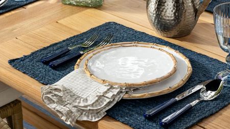 Bamboo plates styled alongside gingham napkin linen, navy placemat, and coordinating navy flatware atop of a wooden dining table