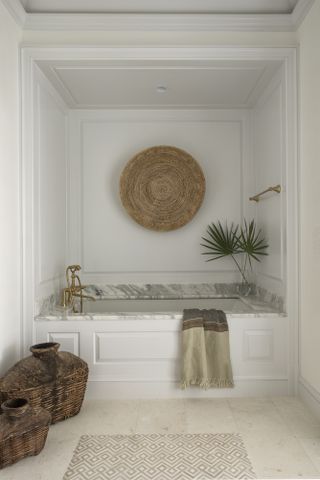 Bath tucked into an alcove with white panelling, stone surface and rattan wall hanging
