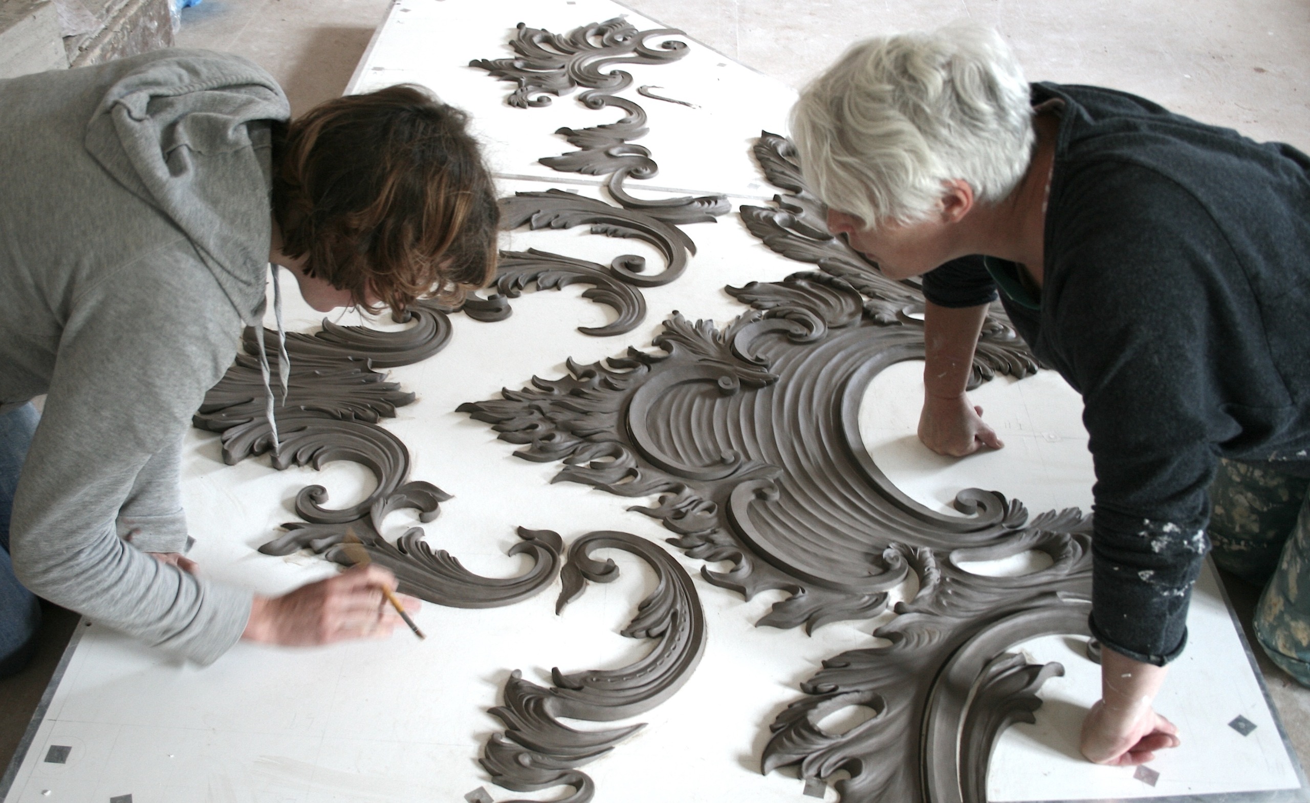Two people bent over a white table covered in plasterwork moulds