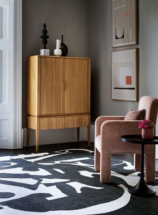 Grey living room with a black and white feature rug and a blush pink chair