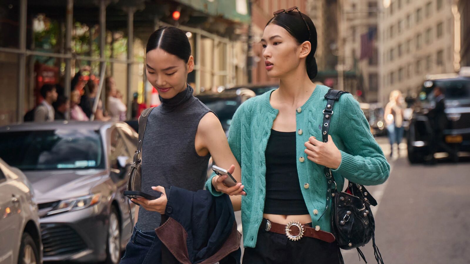 Two Women wear black pants and a basic top and one has a sweater on. 