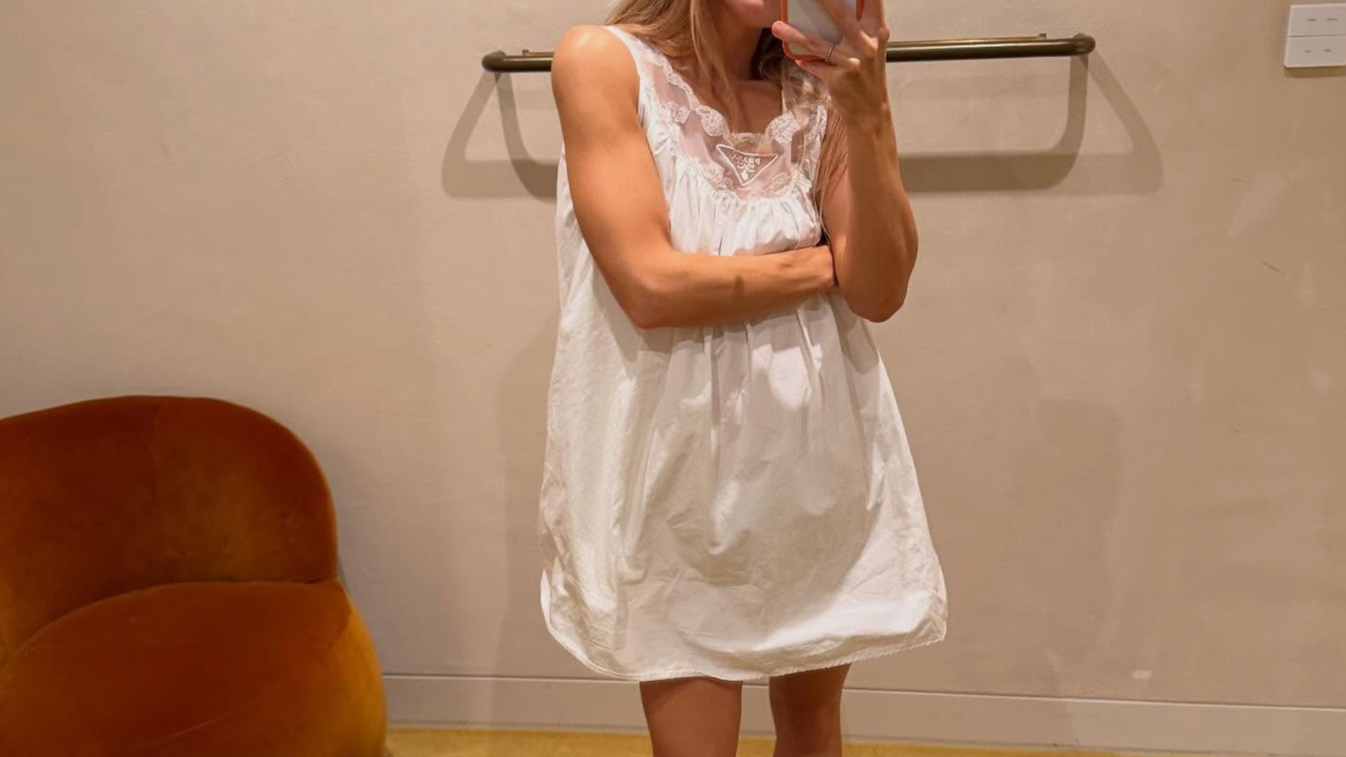 @rachelle.rowlings taking a mirror selfie wearing a white Prada sleep-style dress.