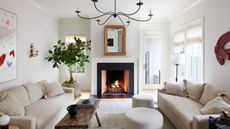 A white living room with white walls and ceiling, two light beige sofas, a vintage wooden coffee table, a neutral rug, and transitional decor. 