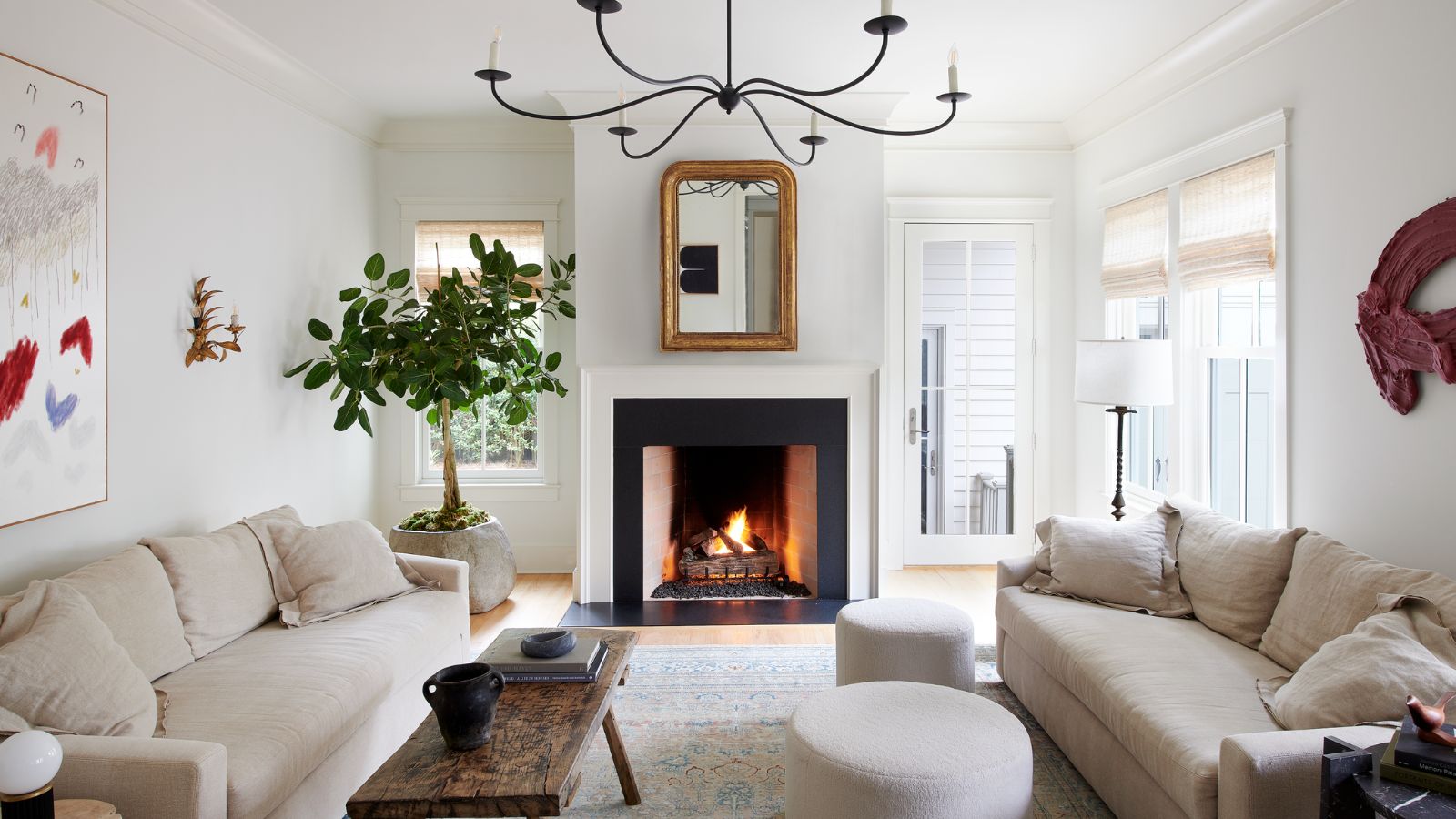 A white living room with white walls and ceiling, two light beige sofas, a vintage wooden coffee table, a neutral rug, and transitional decor. 
