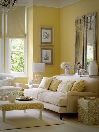 A yellow living room with an off-white sofa and a patterned foot stool