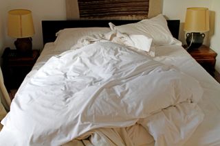 An unmade bed with white bedding