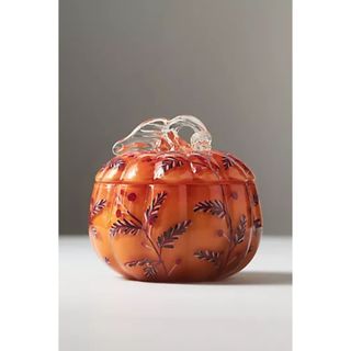 A orange glass pumpkin shaped candle jar with hand painted floral details. 