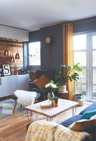 Spillett house: living room with pallet coffee table, wingback chair, grey-blue wall, yellow curtain