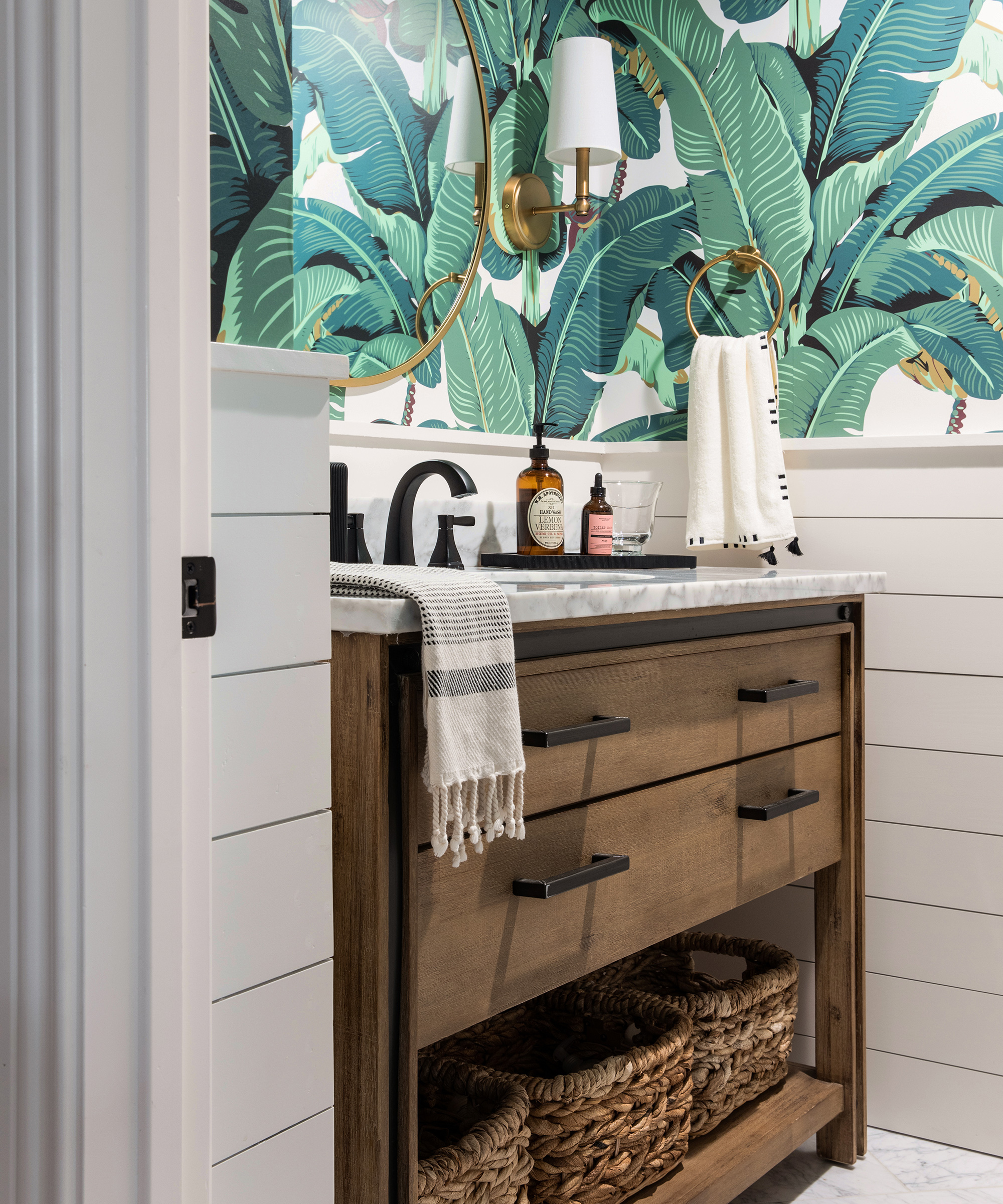 A wooden sink stand below green palm print wallpaper in a powder room