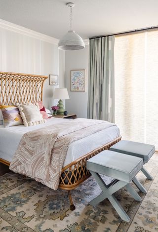 bedroom with bamboo bedframe white striped wallpaper ikat rug two blue stools and pompom pillows