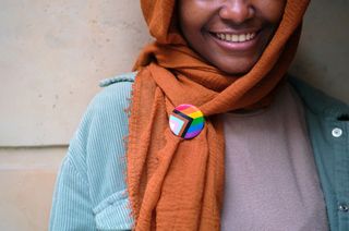 A smiling Muslim woman wearing a lgbtq pin on her clothing