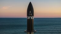 The top of a black rocket stands against a background of rich sea parted in the center by the horizon, and a cool, orange-hued sky. 