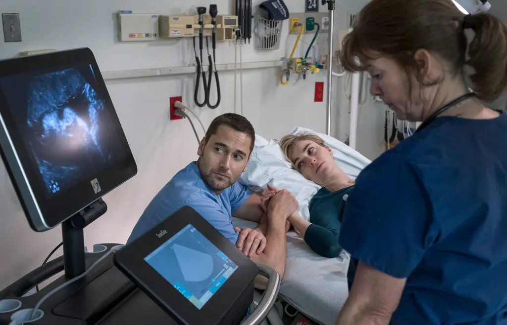 A doctor holds a patient's hand as they look at an ultrasound machine to their left. A nurse (right) operates the machine, in a still from 'New Amsterdam'.