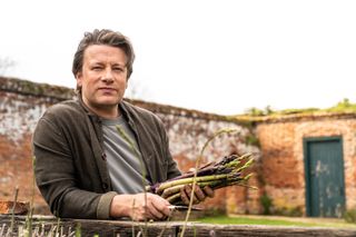 Jamie Oliver holding fresh asparagus in his garden.