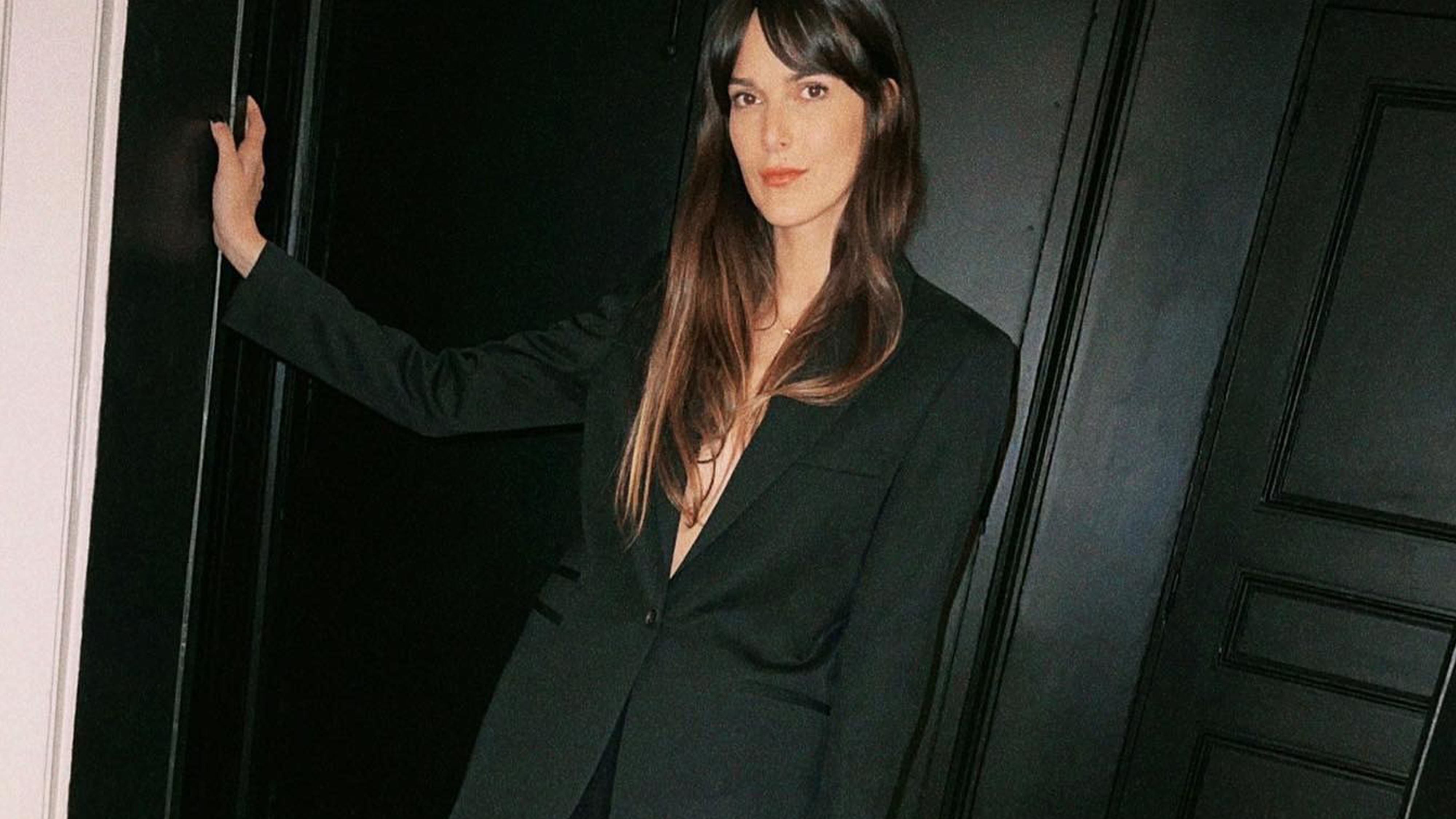 Woman wearing black oversize blazer, standing against door.