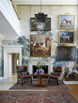 A living area with two large rugs, two armchairs, a mural on the wall, and antique artwork