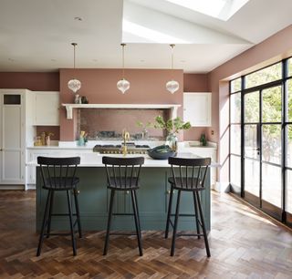 A kitchen extension with green painted island, plaster pink walls, crittall doors and skylights.