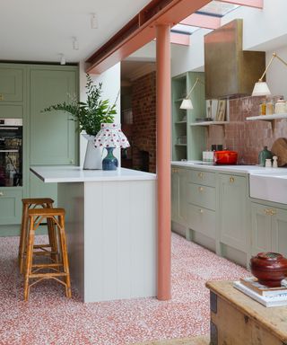 pale green and red kitchen with speckled red floor tiles, pale gree cabinetry small island, white countertops,