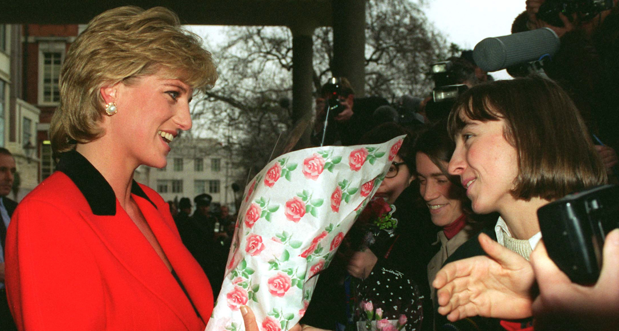 Princess Diana wearing a red suit holding flowers talking to fans