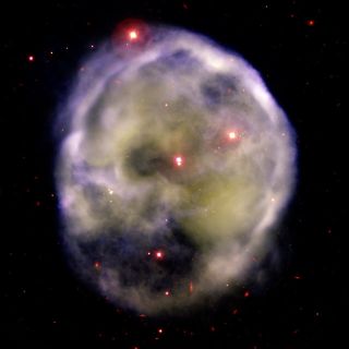 hazy purple and yellow clouds of gas and dust take the form of a skull against a background of red stars.