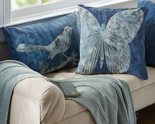 A set of two Batik printed blue scatter cushions with bird and butterfly design in living room on cream-colored sofa