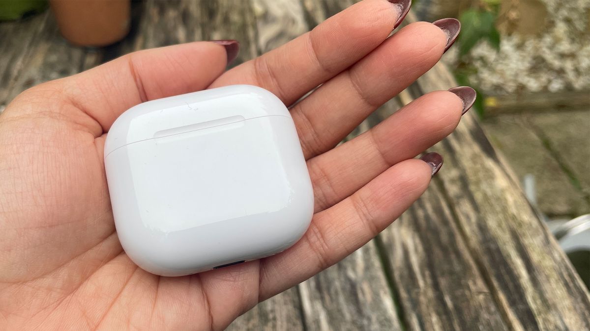 The Apple AirPods 4 with ANC case, closed, held in an open hand in front of a wooden outside surface.