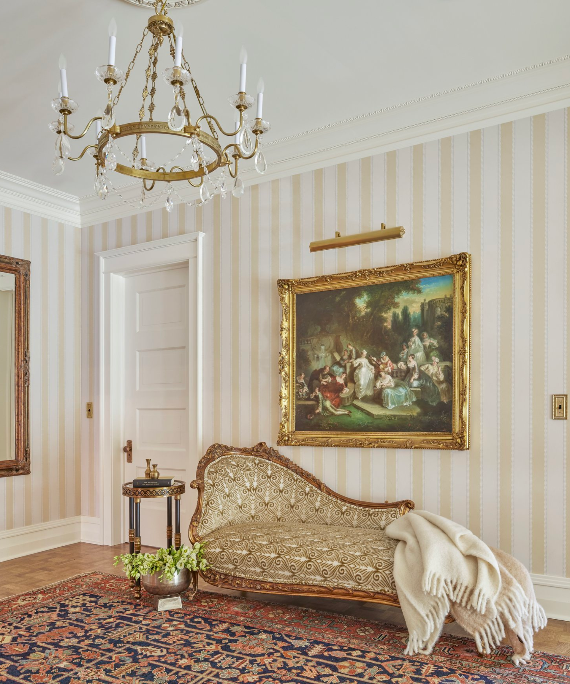 A white living room with a patterned rug, gold chaise longue and a vintage gold picture frame.