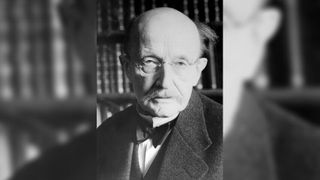 Portrait of an older white man who is bald with round glasses and a mustache. He is wearing a bowtie