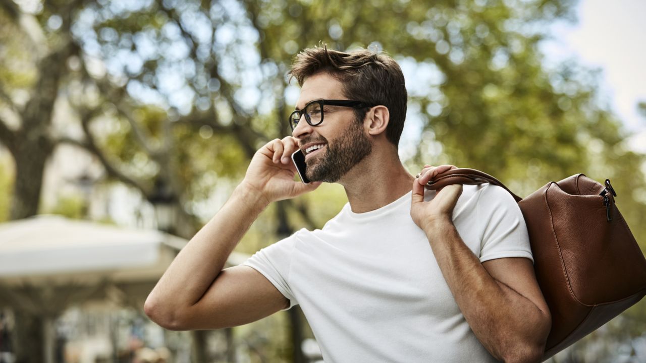 A man walking the the street, walking on the phone and wearing one of the best T-shirts for men