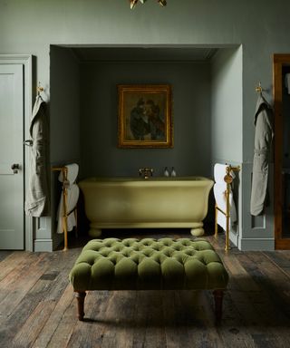 A green bathroom with a freestanding bath and an upholstered green ottoman