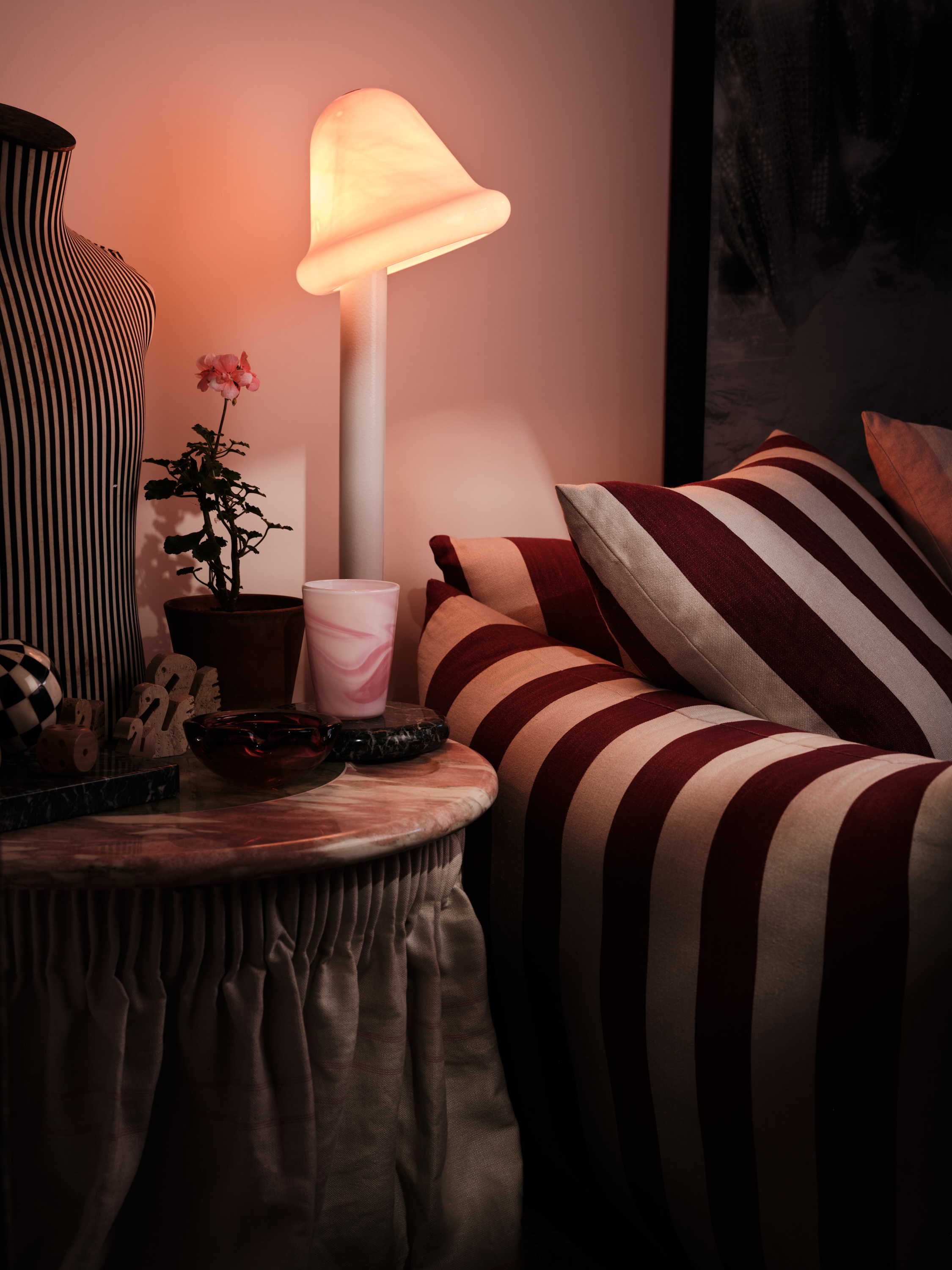 A marble side table, perched beside a striped sofa, with a glass lamp on top