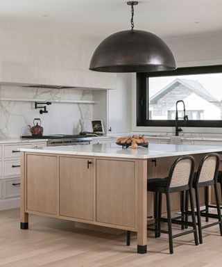 A modern kitchen with marble counters and backsplash, and a large bronze domed light fixture