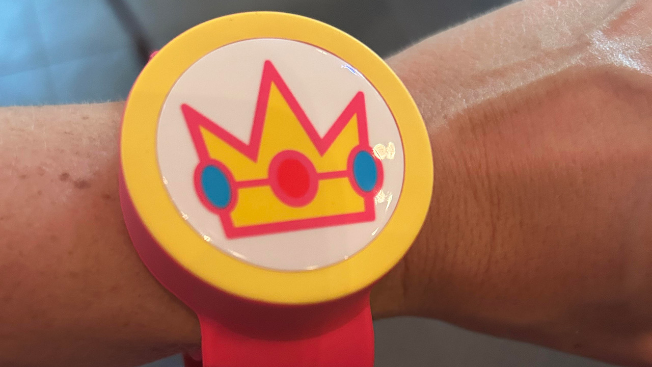 The Princess Peach Power Band at Super Nintendo World Epic Universe is pink and white and yellow with a crown and blue accents.