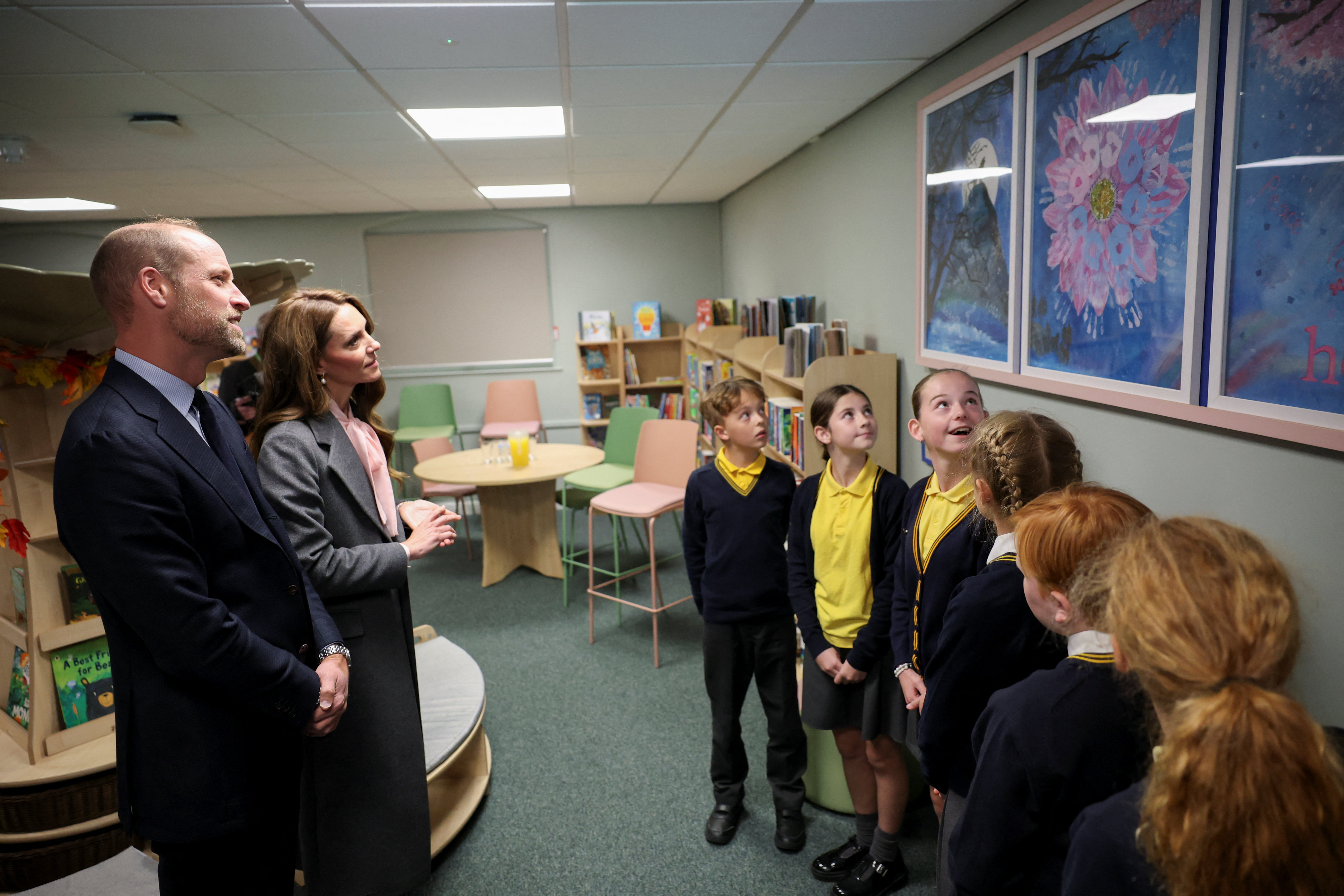Prince William and Kate Middleton talking to school students and looking at pictures on a wall