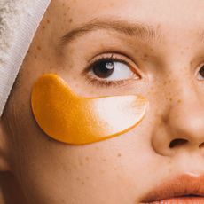 Girl in towel with gold-colored hyaluronic eye mask on her face to treat dark circles