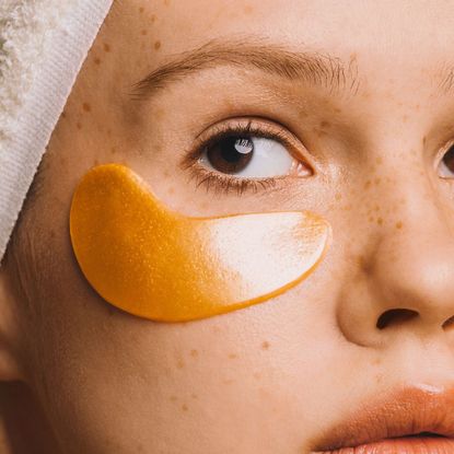 Girl in towel with gold-colored hyaluronic eye mask on her face to treat dark circles