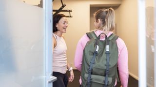Woman enters gym, greeted by a trainer standing by the door