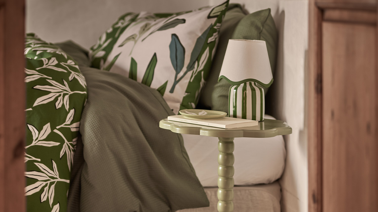 Green &amp; White Stripe Battery Scallop Shade Lamp on green bobbin side table, next to a double bed which has green bedsheets.