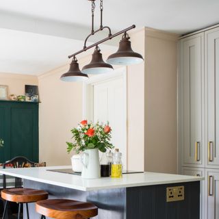 A soft peach-painted kitchen and dining area with a navy blue island with bar stools and pendant bar lighting