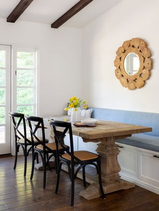 kitchen diner with white walls and wood table with black dining chairs and fitted blue banquette seat with mirror above and french doors