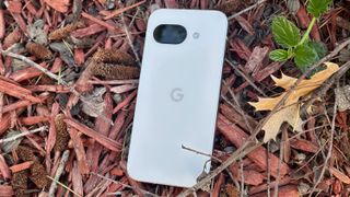 The porcelain Google Pixel 9a sitting on top of bark on the ground.